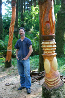 Photo of artist Boomer Dormody next to the totam tree carvings at WildSpring